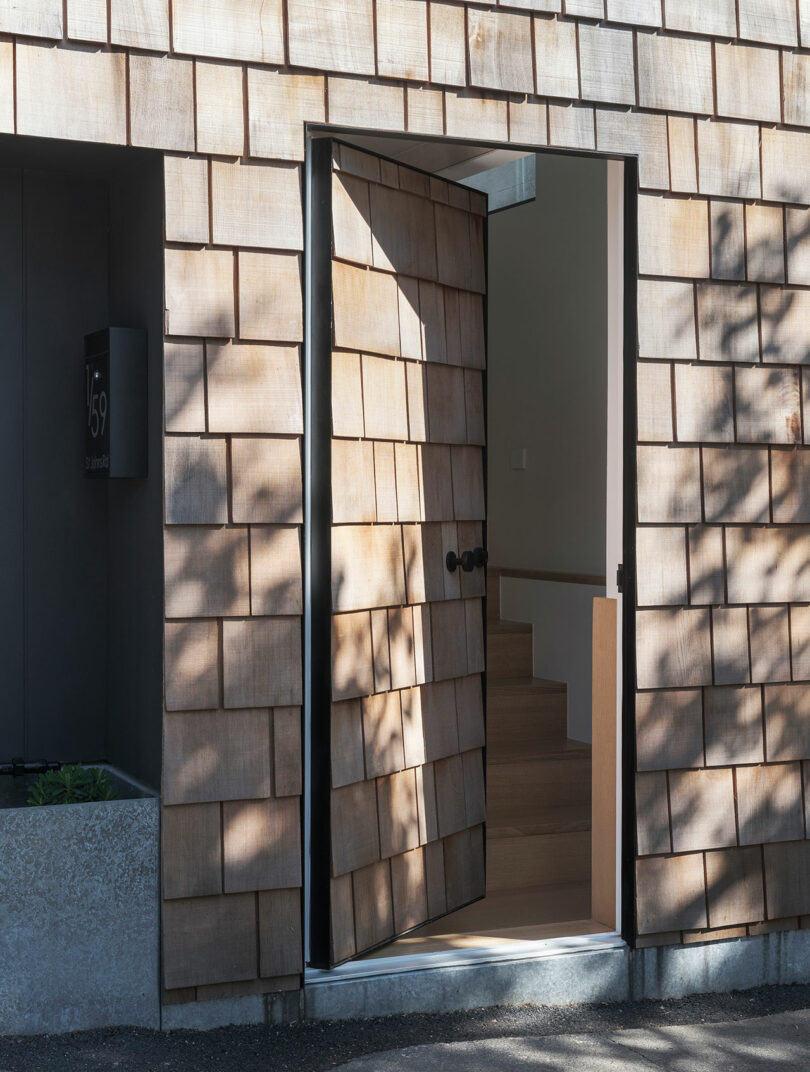 A wood shingle wall with an open door leading to an internal staircase. The door casts shadows outside.